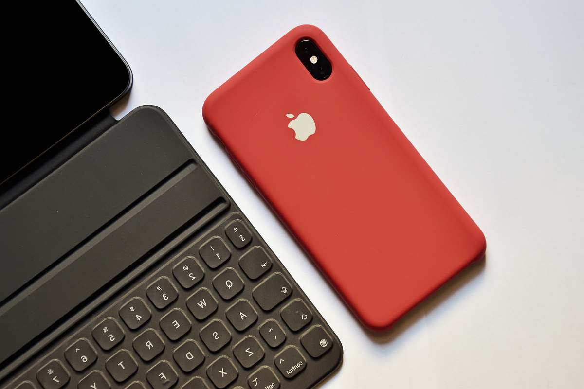 electronics space gray iPhone with red case beside tablet keyboard mobile phone